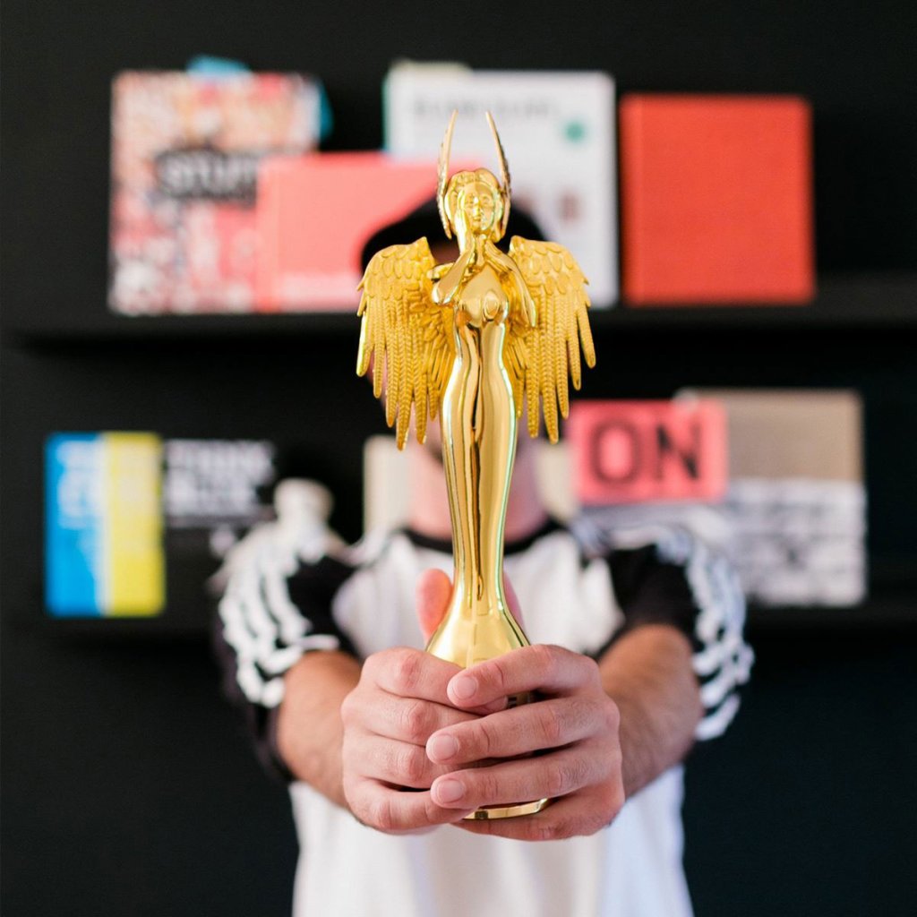 Foto von Tim Hüfner bei dem er einen Design Award in den Händen hält und diesen in die Kamera streckt.