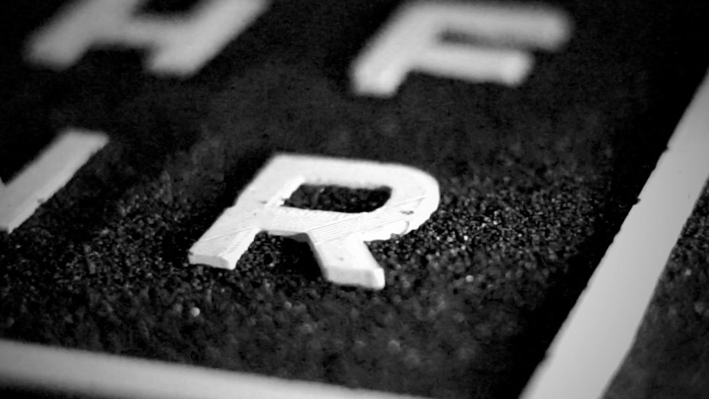 Detailaufnahe des HFNR Logos in Beton gegossen, die Zwischenräume sind mit schwarzem Sand befüllt.