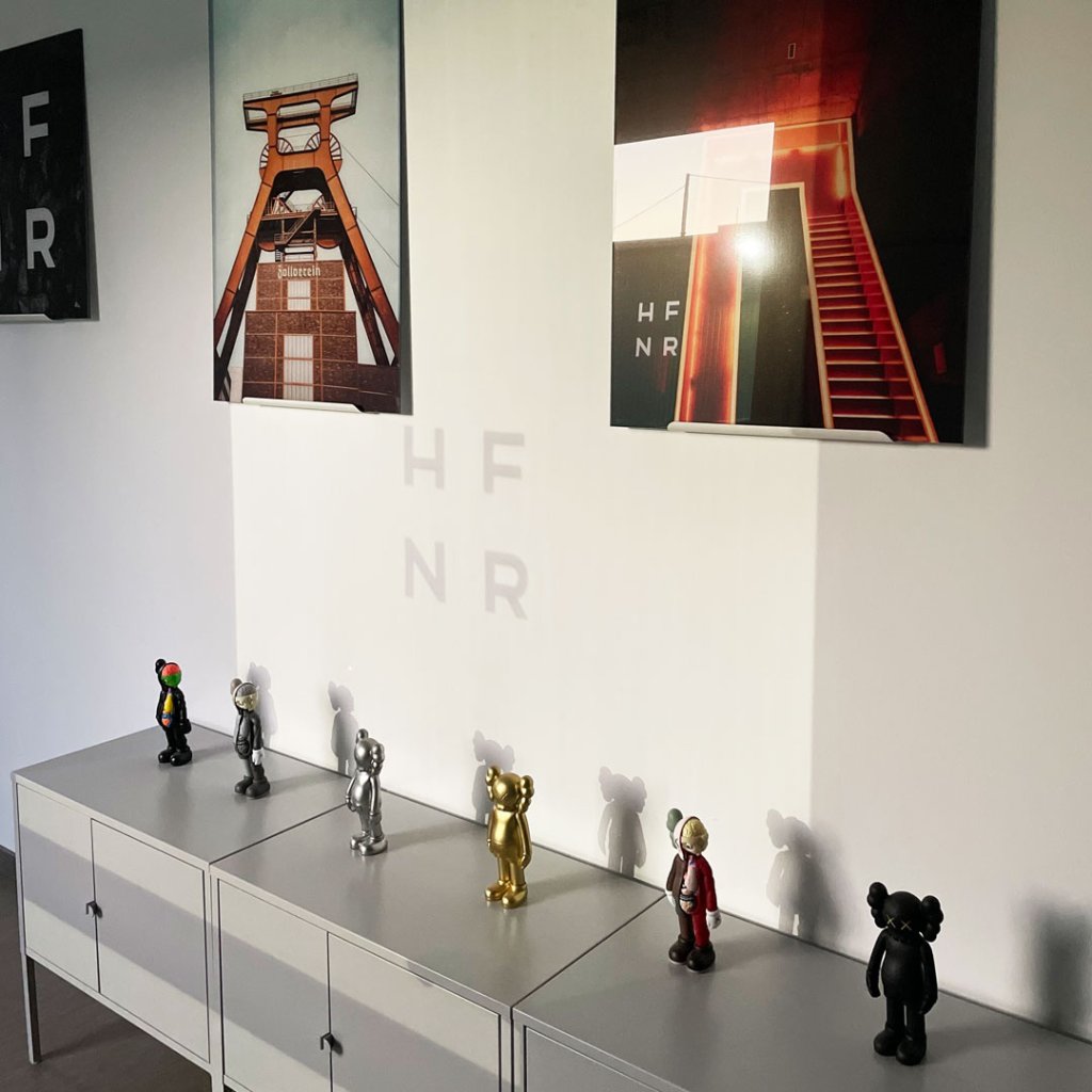 Detailfoto aus der HFNR Hüfner Design Studio, zu sehen sind ein paar Fotoa ander Wand und ein paar Kaws Figuren auf einem kleinen Schränkchen.